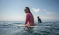 A woman wearing a pink rash vest sitting on a surfboard in the sea