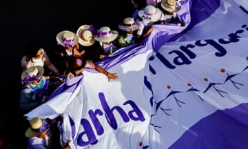 Women in straw hats with purple ribbons seen from above holding a large banner that reads: Marcha das Margaridas