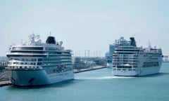 Two cruise ships moored in Barcelona's port, as another begins sailing away