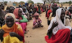 Young Sudanese girls sit on the ground in a desert like environment