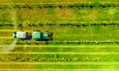 Overhead view of a tractor towing a tank which is spraying pesticide on grapevines