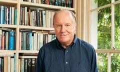 William Boyd in a blue shirt standing in front of a bookcase in his London home.