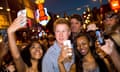 a smiling lookalike prince harry flanked by two young women taking selfies with him