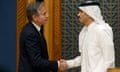 White man in dark suit on right shakes hands with Arab man in white thobe and all-white keffiyeh on right.