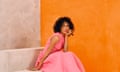 Vinette Robinson wearing a pink dress and lilac mules, sitting on white marbled blocks against an orange backdrop