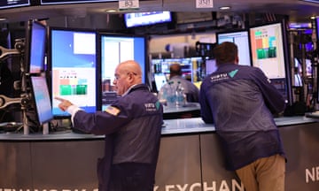 Two men wearing navy jackets look at several screens