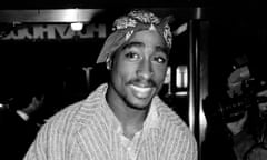 Young Black man, bandana knotted on forehead, pinstripe jacket, smiling in a black-and-white photo.