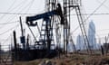 Silhouette of nodding donkey pumping oil with buildings in background