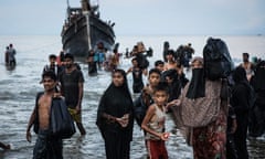 Rohingya men, women and children walk ashore through the water from an overloaded boat