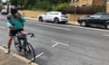 Chris is wearing a helmet and sitting on his bike on the side on a road. He is looking down, holding his phone in one hand and having a drink from a water bottle