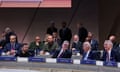 four men sit in chamber with name plates with their countries' names on them