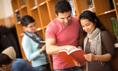 Couple of studying  friends reading book from library<br>J4YHXA Couple of studying  friends reading book from library