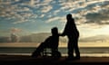 Silhouette of person pushing another person in a wheelchair against a blue sky with clouds