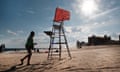 An empty lifeguard chair on a beach with silhouettes of people and buildings in background