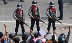 Armed anti-riot police stand guard as demonstrators flash the three-finger salute, a symbol of resistance, during a protest against the military, in Naypyitaw, Myanmar