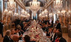 Dignitaries sat at a long banquet table stretching into the distance, with flower arrangements and candles on the table, and chandeliers reflected in the mirrored walls