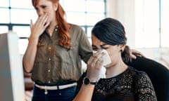 Woman sneezing beside a work colleague
