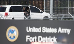 officer with a gun peaking out of a white car in front of a sign reading United States Army Fort Detrick