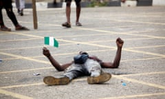 A protester holds the Nigerian flag as he lays on a road near the Lagos governor’s office during a protest against police brutality.