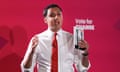 Anas Sarwar gesticulates as he holds Scottish Labour's manifesto which has him and Keir Starmer on the front cover. Sarwar is standing against a red background with a 'vote for change' Labour logo