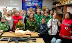 A screenshot of  a deleted image showing Russian Red Cross staff posing with Kalashnikov rifles at a military event for children.