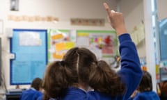 A child with two ponytails raises her hand in a classroom