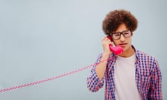 Portrait of young man talking on vintage telephone<br>Serious young funny man talking on the pink telephone, isolated on blue wall background