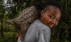 A young black woman with a pangolin sitting on her shoulder smiles at the camera