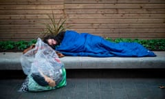 A homeless man sleeps in central London on a concrete bench with his belongings in a transparent bin liner