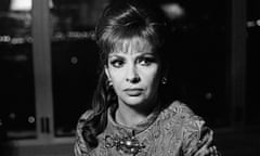 Gina Lollobrigida, with long hair and some hair puffed out above a slight fringe, in a brocade jacket with a big horizontal brooch, looking serious