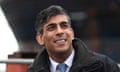 Rishi Sunak sitting with a hot drink and appearing to gaze into the distance, with a ship in the background