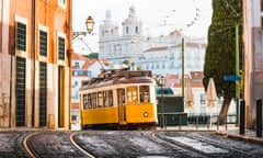 A yellow tram in Lisbon, Portugal, with tramlines in the foreground and ornate buildings in the background