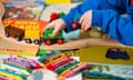 A toddler playing with  a wooden train set with crayons and children’s books nearby