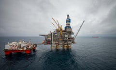 view across Mariner oil field off Aberdeen, Scotland showing large oil rig structures including cranes and drilling equipment; the sea and sky are both dark grey, and a red oil tanker is seen in the background