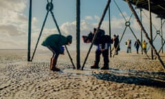 Volunteers on the beach under the pier examine a pool of water searching for living creatures