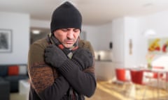 Portrait of a man wearing a beanie, scarf and woollen gloves shivering from cold inside his home