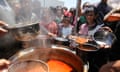 Children holding pots and pans gathering round a huge pot of soup or stew,