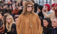 A model wearing tan-coloured boho-inspired clothes poses on the catwalk as the audience looks on