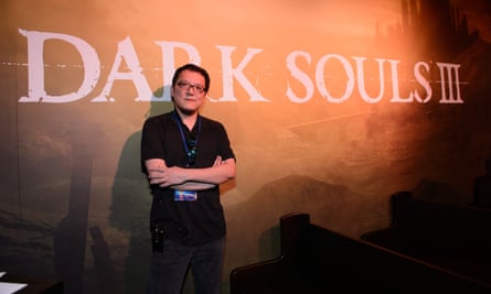 Hidetaka Miyazaki at E3 expo, standing in front of a Dark Souls poster.