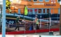 Three men accompany a person on a stretcher on a quay with an RNLI lifeboat in the background.