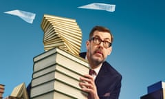 Richard Osman peeking out from behind a giant stack of books