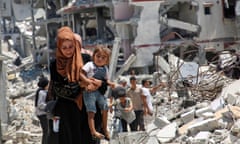 A Palestinian woman holds her daughter as she walks past the rubble of homes in Khan Younis.