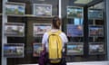 A woman wearing a backpack looks at advertisements in an estate agent window