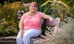 Janet Williams, in a lacy short-sleeved top and wearing glasses, on a bench in her garden