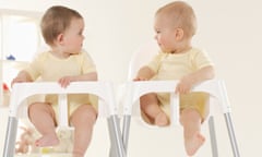 Two babies sitting in highchairs, looking at each other