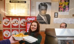 A woman hands a box of chips over the counter with a poster of Cary Grant on the wall behind