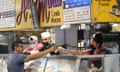 Money is exchanged at a food stand while workers wear face masks inside Grand Central Market on Wednesday, July 13, 2022, in Los Angeles. Falling gas prices gave Americans a slight break from the pain of high inflation last month, though the surge in overall prices slowed only modestly from the four-decade high it reached in June. And even as gas prices fall, inflation in services such as health care, rents and restaurant meals is accelerating. (AP Photo/Marcio Jose Sanchez)