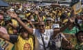 A crowd of people, many wearing the ANC's colours of yellow and green, attend a march. Some hold their hands out while others hold placards