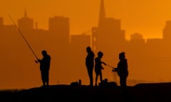 With the San Francisco skyline behind them, people fish off a jetty