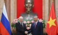 Vladimir Putin and To Lam shake hands between the Russian and Vietnamese flags and in front of a large bust of Ho Chi Minh